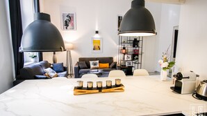 Una sala de estar moderna con una isla de mármol, dos lámparas colgantes, un sofá con cojines, una mesa de centro con velas y una estantería.