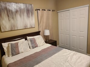 Ein Hotelzimmer mit Bett, Nachttisch, Lampe, Schrank und einem großen abstrakten Gemälde an der Wand.