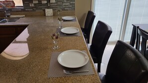 Una cocina con encimeras de granito, un comedor con sillas negras y una ventana con persianas.