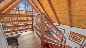 Interior de madera con techo inclinado, una escalera y vistas a árboles otoñales.