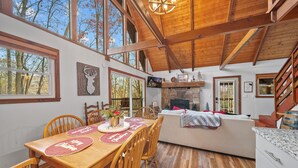 Una mesa de comedor de madera con sillas, una chimenea y un sofá en una habitación amplia con techos altos y ventanas grandes.
