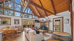 Amplia sala de estar con techos altos, vigas de madera, chimenea y zona de comedor con mobiliario de madera.