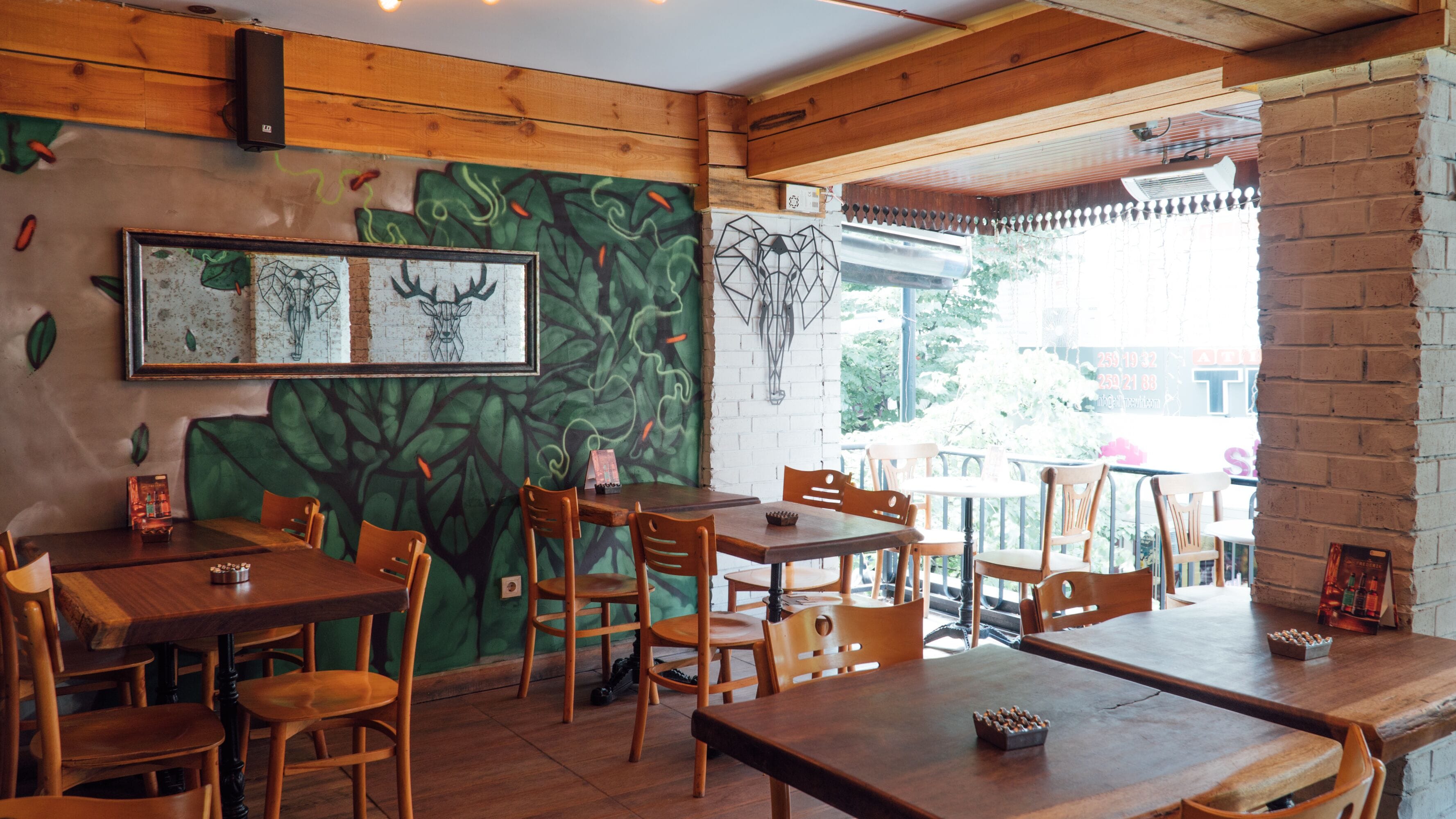 Un interior de restaurante con mesas y sillas de madera, un mural en la pared y vistas al exterior.