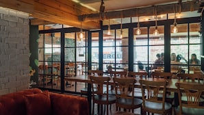 A restaurant interior with wooden tables and chairs, hanging light bulbs, and large windows with views of the street. - Barkod Hotel (Istanbul)