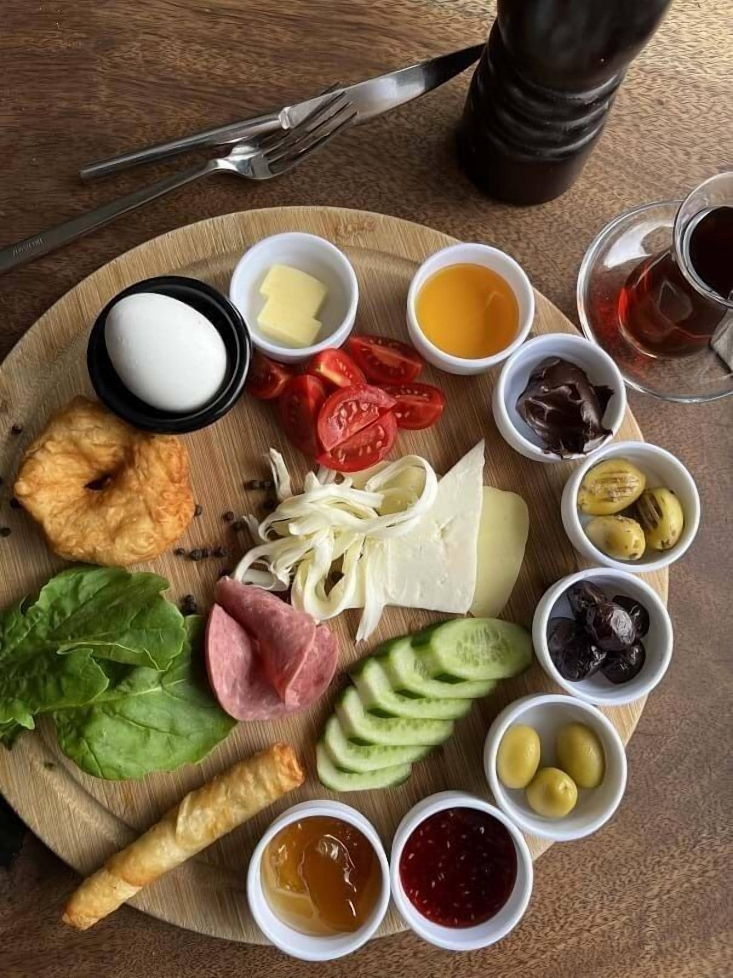 A wooden board with various food items including cheese, tomatoes, olives, and condiments.
