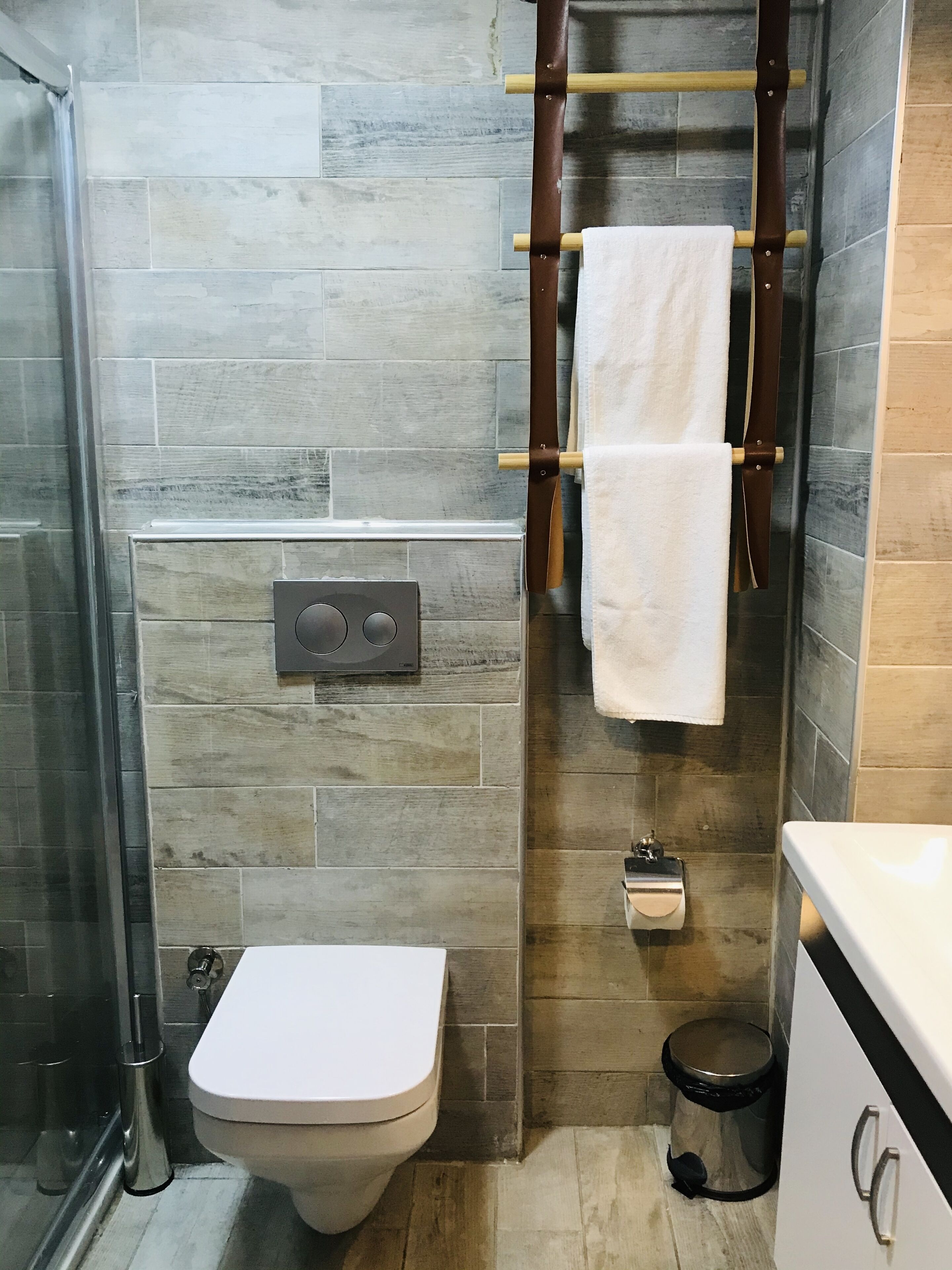 A bathroom with a toilet, a bidet, a towel rack, and a trash bin.