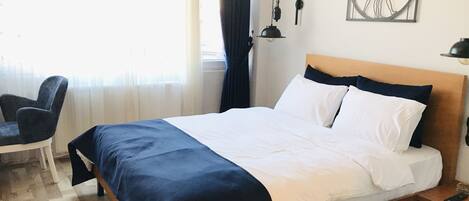 Una habitación de hotel con cama, una silla, una lámpara de pared y una ventana con cortinas.