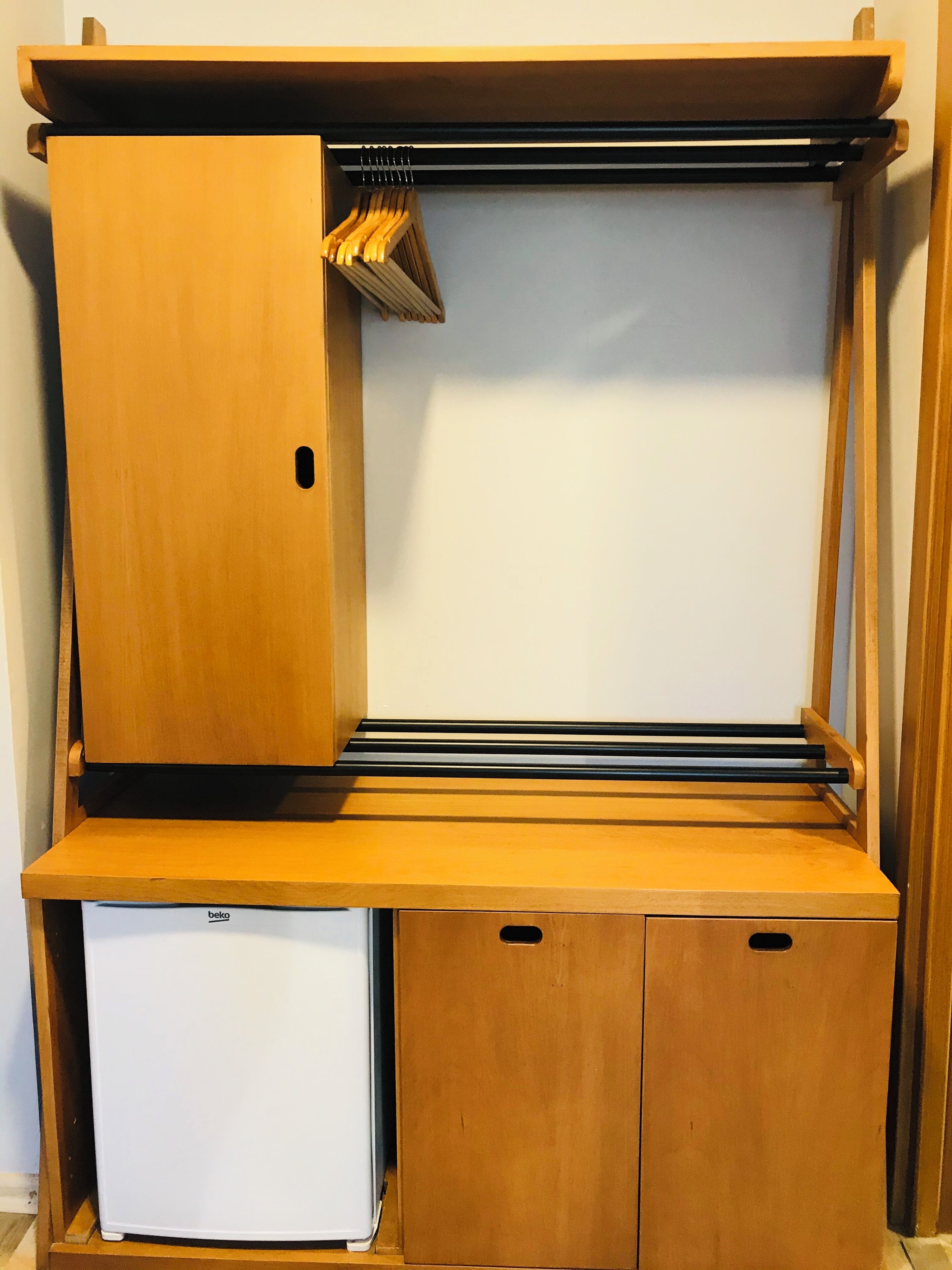 A compact wooden room with a built-in wardrobe, a small white refrigerator, and a shelf.
