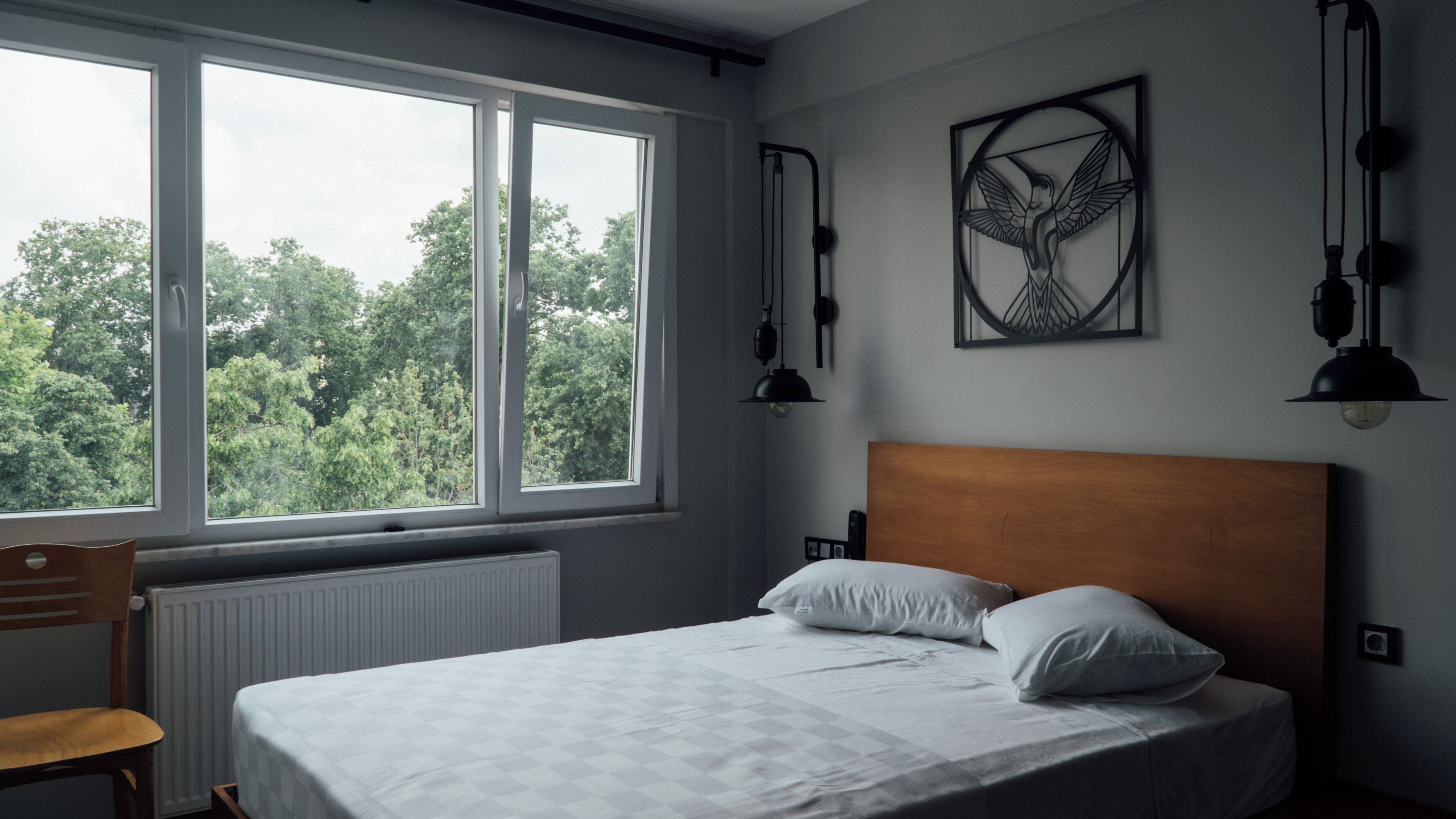 A bedroom with a bed, a chair, a window, and a wall-mounted artwork.