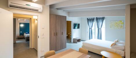 A modern hotel room with a wooden table, a bed, a TV, and a bathroom visible through an open door.
