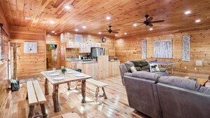 Ein Holzblockbau-Innenraum mit Essbereich, einer Couch, einer Küche und einem Deckenventilator.