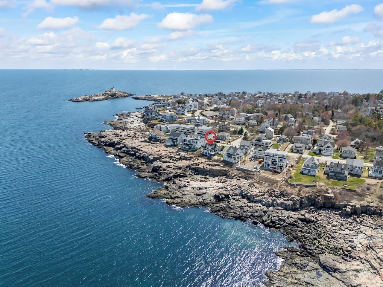 A coastal town with houses along the rocky shoreline, a lighthouse, and a clear view of the sea.