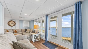 Un salón acogedor con un sofá, una mesita con una lámpara y vistas al mar a través de amplias ventanas.