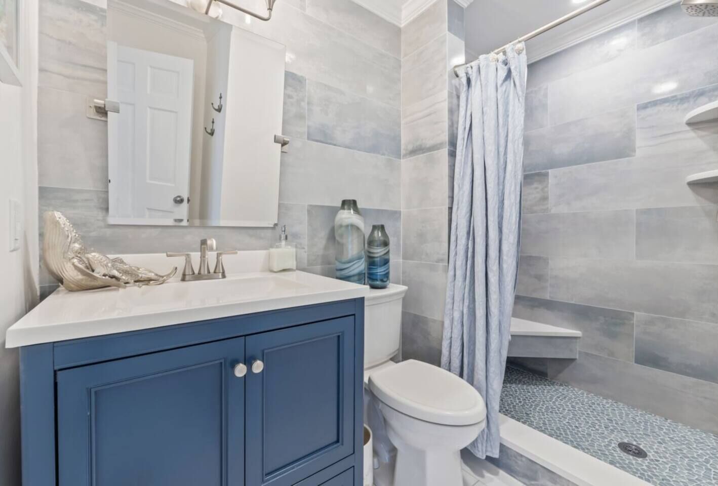 A bathroom with a white toilet, a blue vanity, a shower with a curtain, and marble walls.