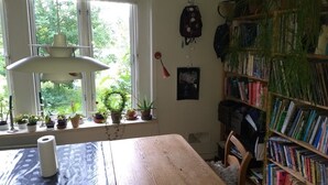 Ett rum med ett träbord, en bokhylla och ett fönster med växter.