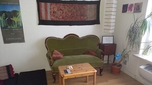 Ett vardagsrum med en grön soffa, ett soffbord i trä, en mönstrad matta och en krukväxt.