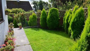 A well-maintained garden with a neatly trimmed lawn, a wooden fence, and potted plants along the pathway. - Simdde Wen -  a bungalow that sleeps 6 guests  in 3 bedrooms (Beaumaris)