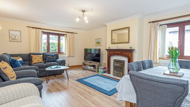 A living room with a sofa set, a television, a fireplace, and a dining area with a table and chairs. - Simdde Wen -  a bungalow that sleeps 6 guests  in 3 bedrooms (Beaumaris)