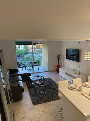 Relax in a spacious living area with a comfortable sofa and glass coffee table, opening to a balcony with city views.