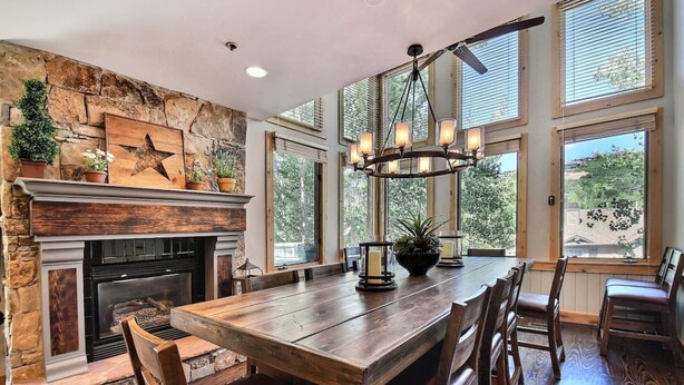 Un comedor con una mesa de madera, sillas, chimenea y ventanas amplias.