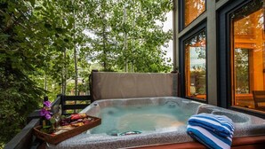 Un jacuzzi con un banco de madera, rodeado de follaje, y una ventana con vistas a árboles.