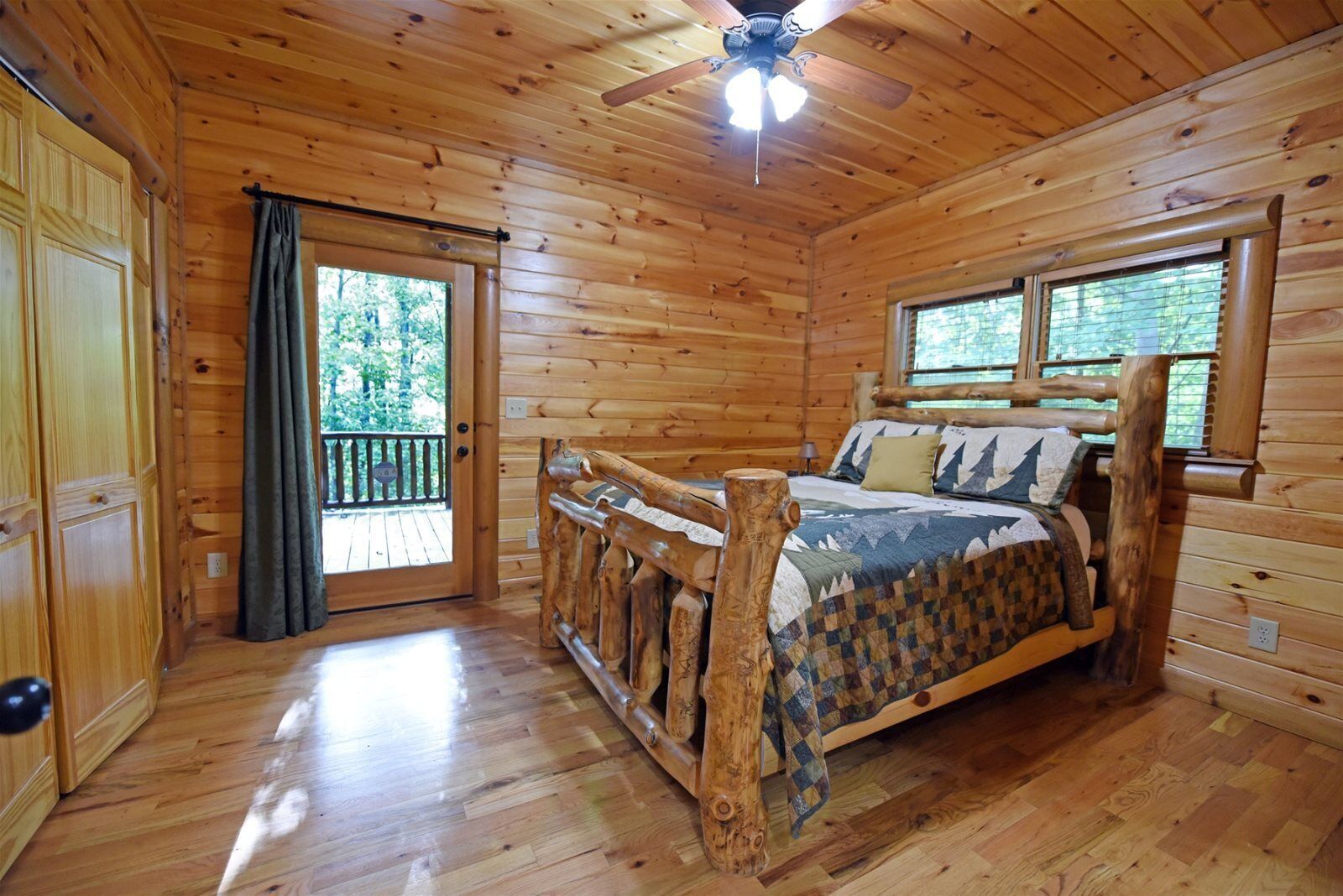A wooden cabin bedroom with a bed, a ceiling fan, and a balcony.