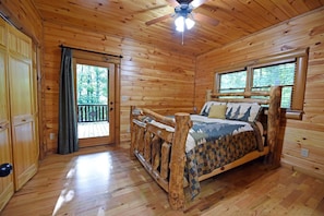 A wooden cabin bedroom with a bed, a ceiling fan, and a balcony. - Shielded Haven (Morganton)