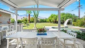 Un patio exterior con piscina, muebles blancos y vistas a montañas.