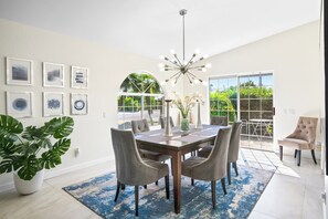 A dining area with a table, chairs, a chandelier, and a large window with a view of greenery.