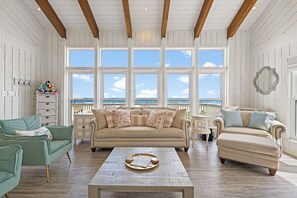 Ein geräumiges Wohnzimmer mit großem Fenster, einem beigefarbenen Sofa, einem grünen Sessel und einem Holztisch.