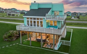 A two-story house with a balcony, a hot tub, and a deck with string lights.