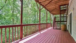 Une terrasse en bois couverte, dotée d’une rambarde rouge, d’un escalier en bois et d’un tonneau.