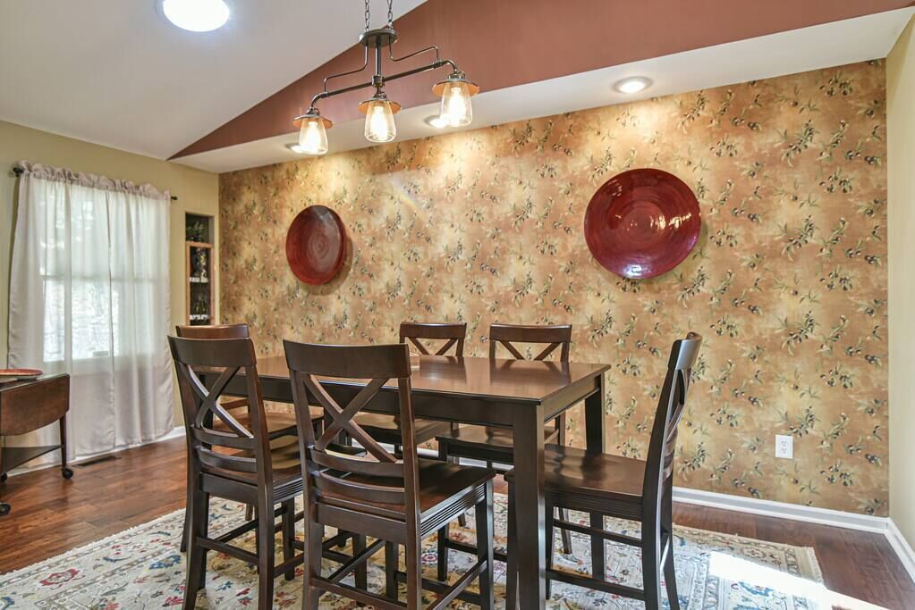 A dining area with a wooden table and chairs, a floral wallpaper, and a chandelier.
