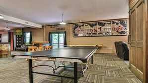 Une table de billard dans une pièce dotée d’un tapis à motifs, de meubles en bois et d’un mur orné d’une enseigne décorative.