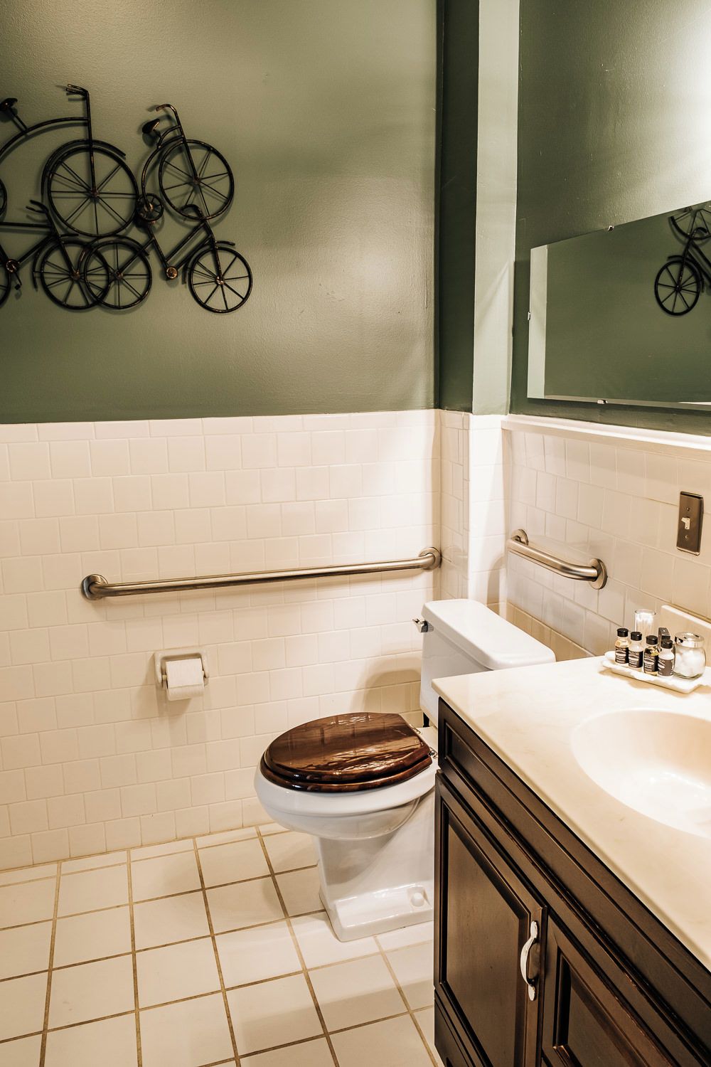 Un bagno con il water bianco, uno sgabello in legno, un lavandino con uno specchio e una decorazione a forma di bicicletta appesa al muro.