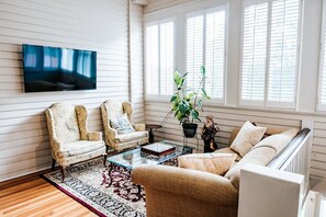 Una sala de estar con dos sillones, un sofá, una mesa de centro, un televisor y un ventanal con contraventanas.
