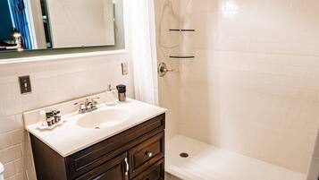 Un bagno con un lavandino bianco, un mobile vanitario in legno scuro e uno spazio doccia.