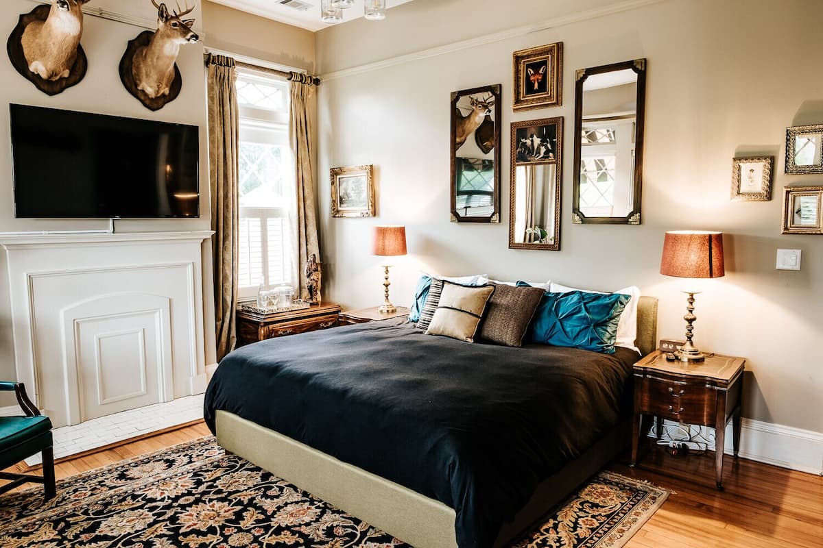 A bedroom with a large bed, a TV mounted above it, and a fireplace.