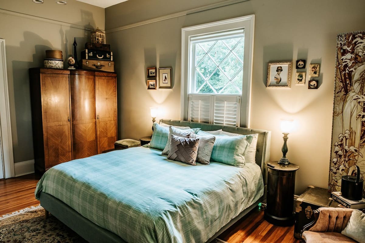 A bedroom with a bed, wooden wardrobe, and a window with blinds.