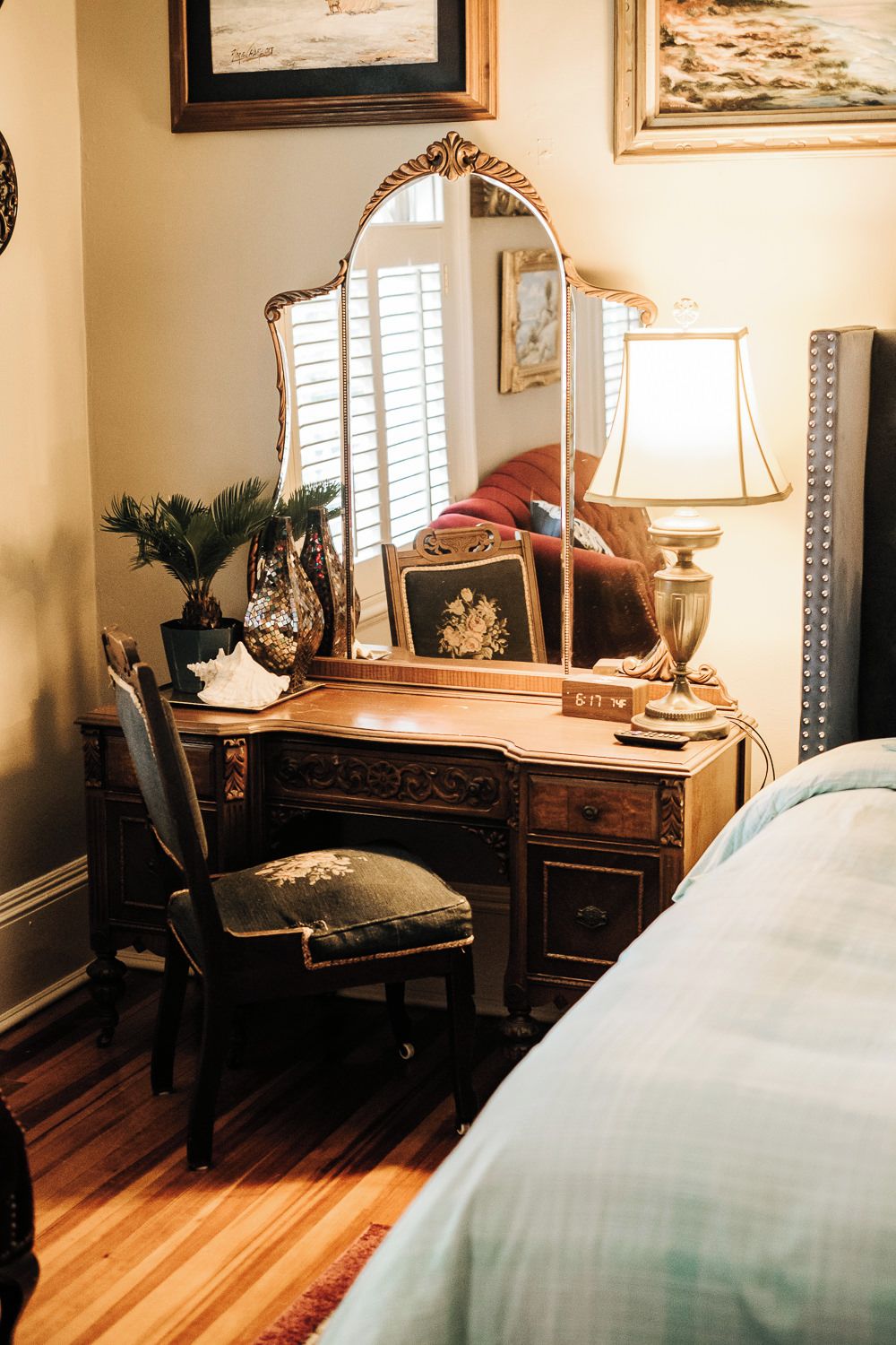 A bedroom with a wooden desk, a chair, a bed, a mirror, a lamp, and a framed picture on the wall.