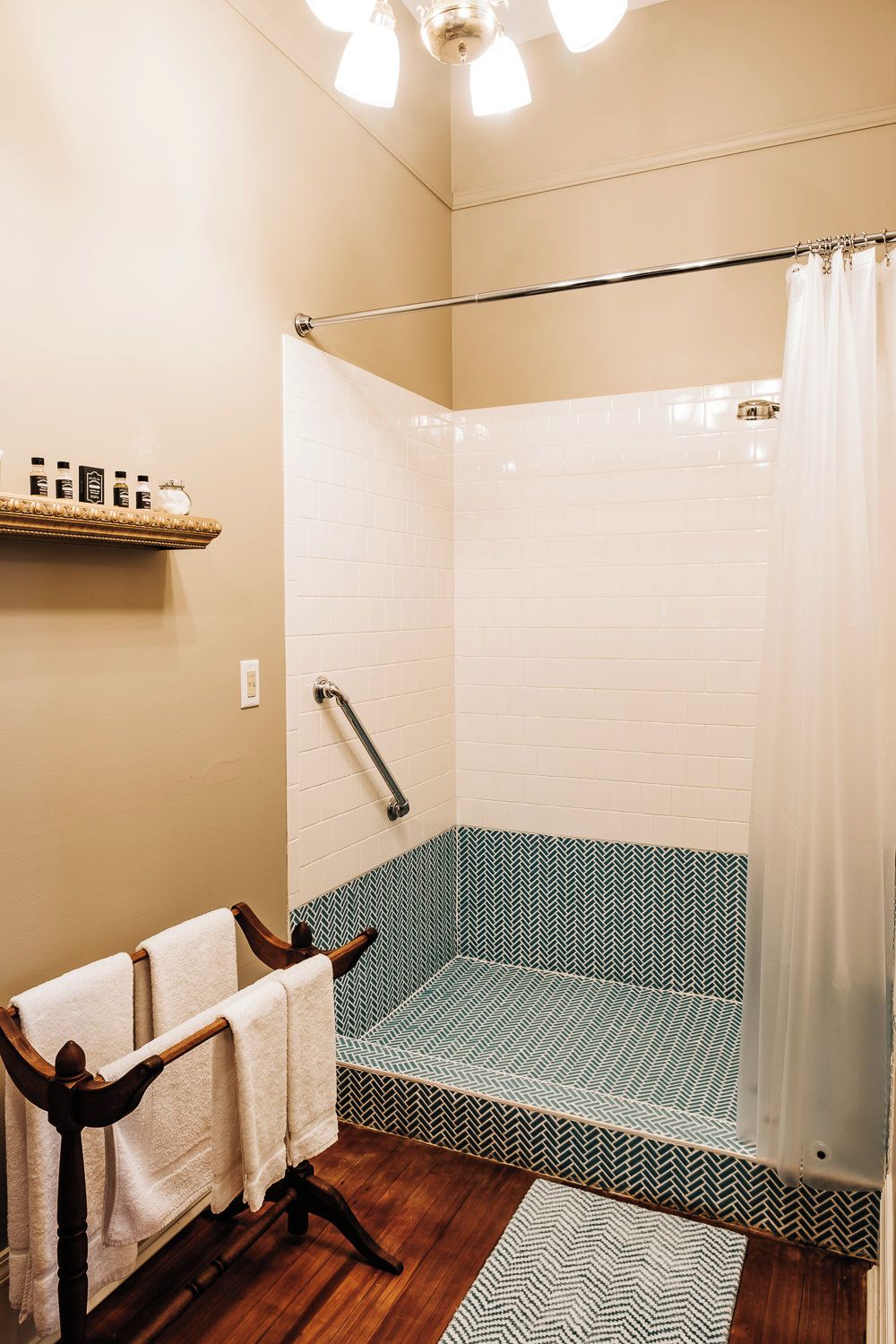 A shower with a white tiled wall, a wooden floor, and a patterned shower floor.
