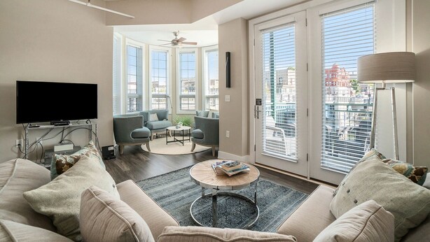 Un salon moderne doté d’un téléviseur à écran plat, d’un canapé, d’une table basse et offrant une vue sur la ville grâce à de grandes fenêtres.