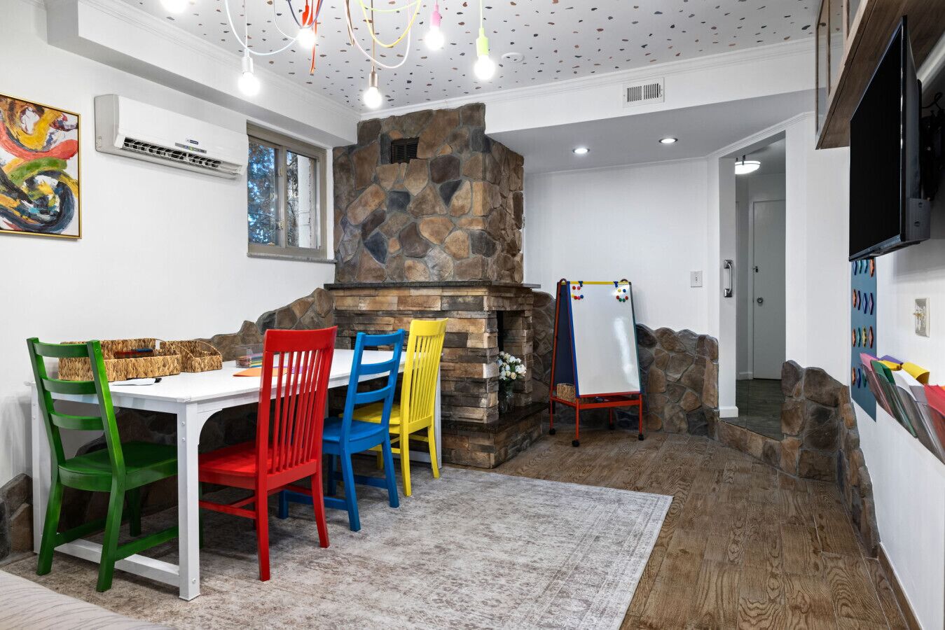 A dining area with a stone fireplace, colorful chairs, and a whiteboard.