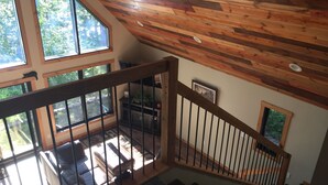 Un escalier avec des rampes en bois menant à un balcon doté de grandes fenêtres, d’une cheminée et offrant une vue sur l’extérieur.