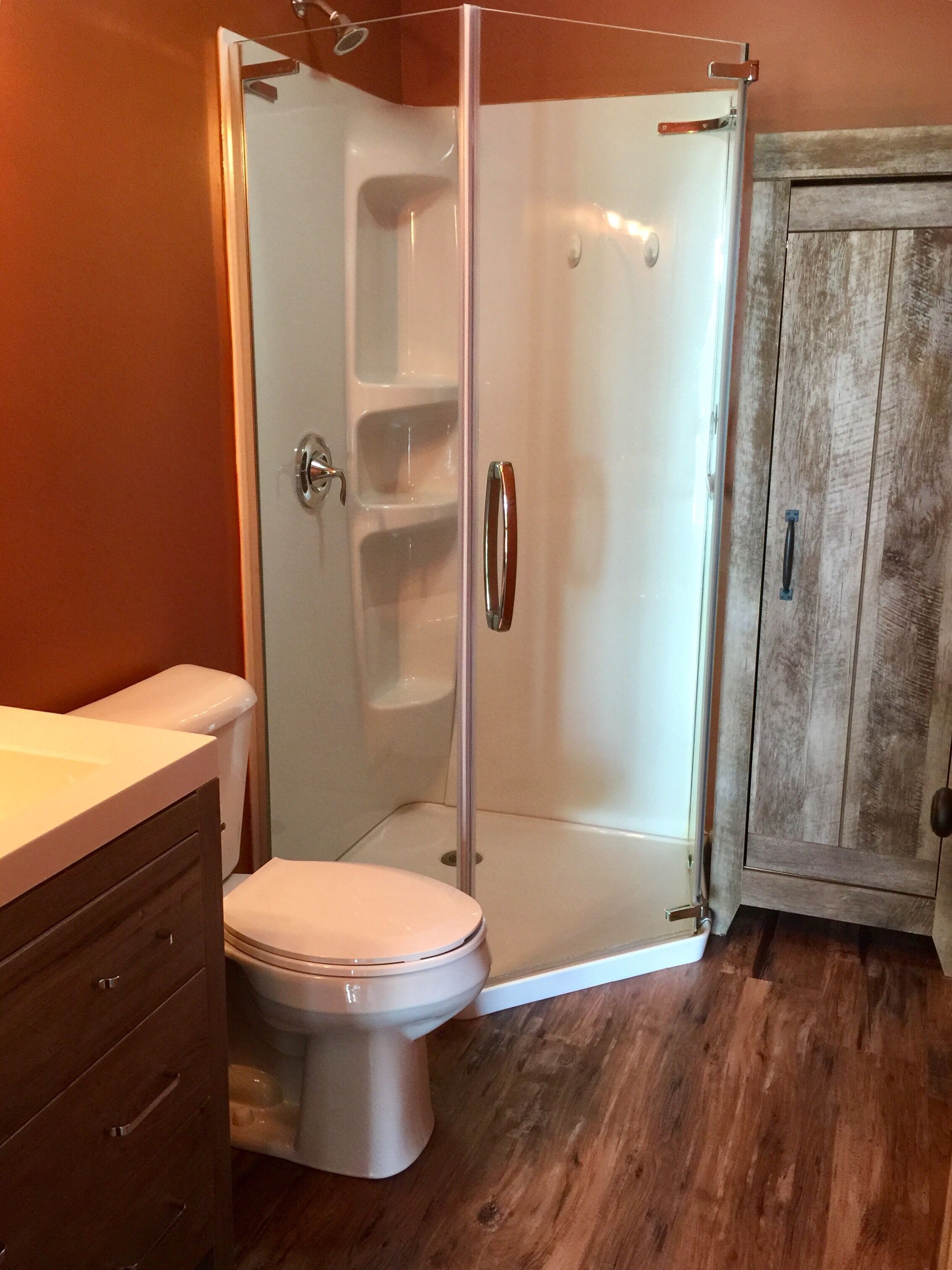 A bathroom with a glass-enclosed shower, a toilet, and a wooden cabinet.