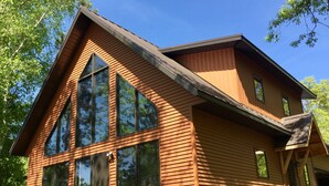 Une maison moderne en bois, dotée de grandes fenêtres et d’un toit à pente.