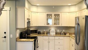 Una cocina con armarios blancos, un refrigerador de acero inoxidable, un microondas y una panificadora sobre la encimera.