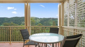 Ein Balkon mit Glastisch und Stühlen, der Blick auf einen bewaldeten Hang bietet.