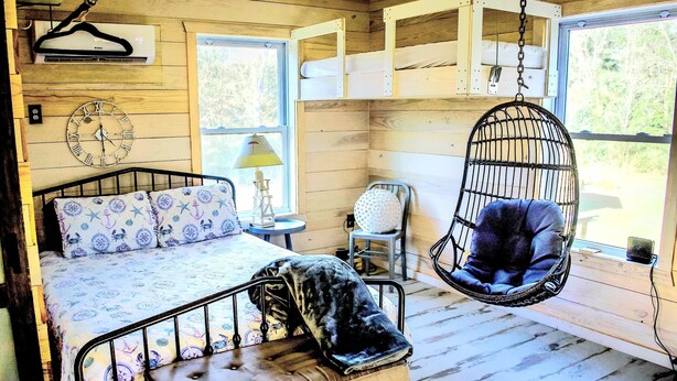 A bedroom with a bed, a hanging chair, a bedside table, and a window.