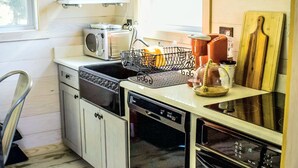 A compact kitchen with a dishwasher, a microwave, a toaster, and a sink. There is a wooden cutting board and a kettle on the counter.